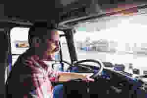 Glücklicher Lastwagenfahrer, der mit breitem Lächeln in der Führerkabine sitzt.