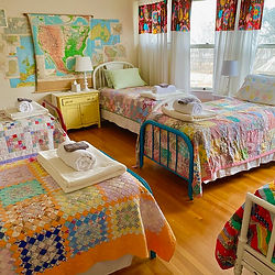 Cozy bedroom with three beds, colorful quilts, and a large map on wall.