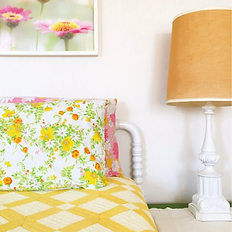 Bedroom with floral pillow, yellow quilt, framed flowers, and a lamp.