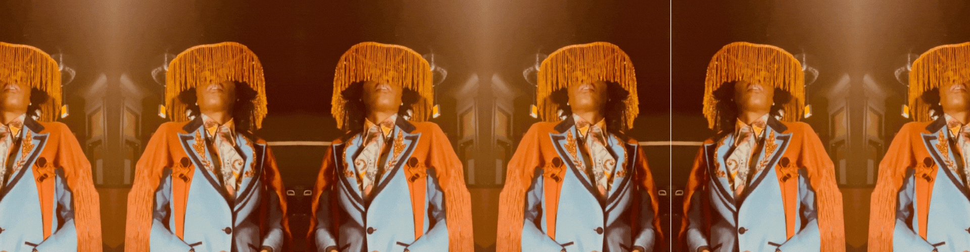 Po'Chop in Costume. Face is concealed by dangling orange fringe. Drag King costume. Po'Chop