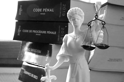 Image en noir et blanc d'une statue de Lady Justice, avec 4 code pénal en arrière plan. La statue, représentant une femme tenant une balance de justice d'une main et une épée de l'autre, a les yeux bandés. Cette représentation symbolique évoque les principes de justice, d'équité et de droit dans le système judiciaire