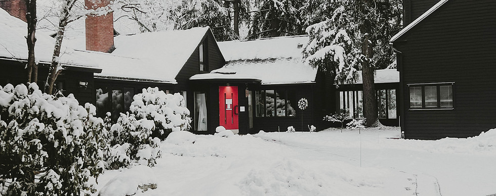 Dark house with prominent red door, surrounded by snowy winter landscape.