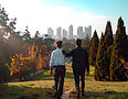 Two men walking through a park with one person holding a shoulder with a city back