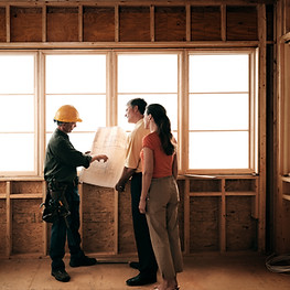 Custom home, new home site husband and wife meeting with builder to go over home plans and blueprints for new construction and remodeling projects where they look at home plans and begin estimating, quoting and project management process.