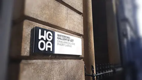 a sign for the waterford gallery of art hangs on a stone wall