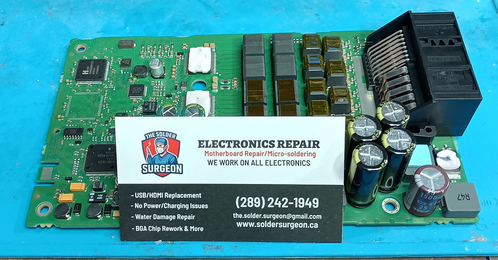 A close-up workbench photo of a BMW logic 7 audio amplifier circuit board prepped under a microscope for component-level repair, showing exposed surface-mount capacitors and power regulation chips on the PCB substrate.