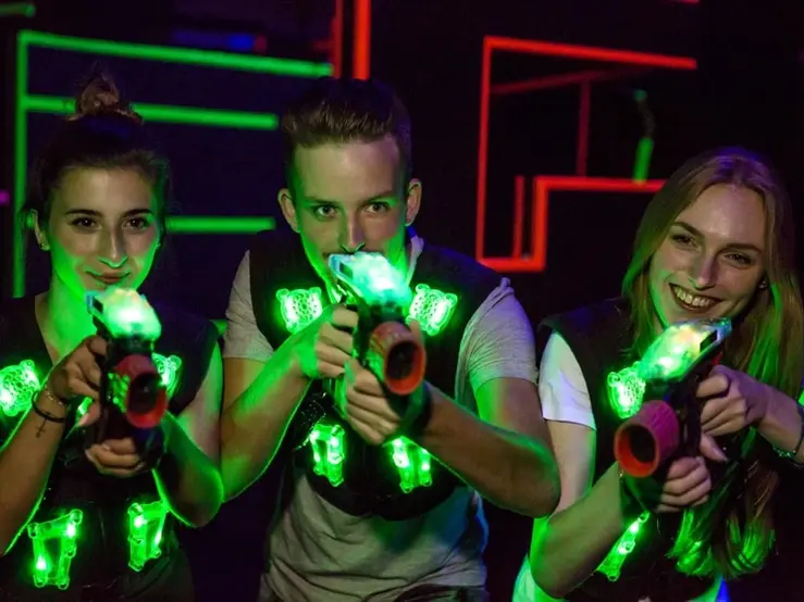 Gruppe junger Leute beim Lasertag-Spiel in einer farbig beleuchteten Arena mit leuchtenden Westen und Spielgeräten.