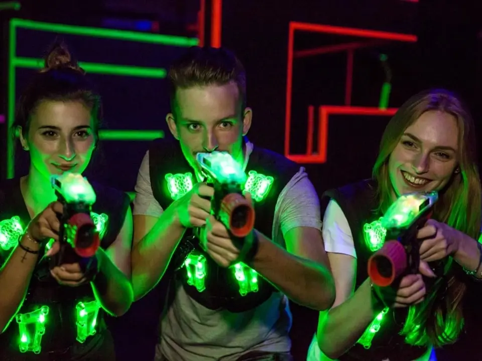Gruppe junger Leute beim Lasertag-Spiel in einer farbig beleuchteten Arena mit leuchtenden Westen und Spielgeräten.