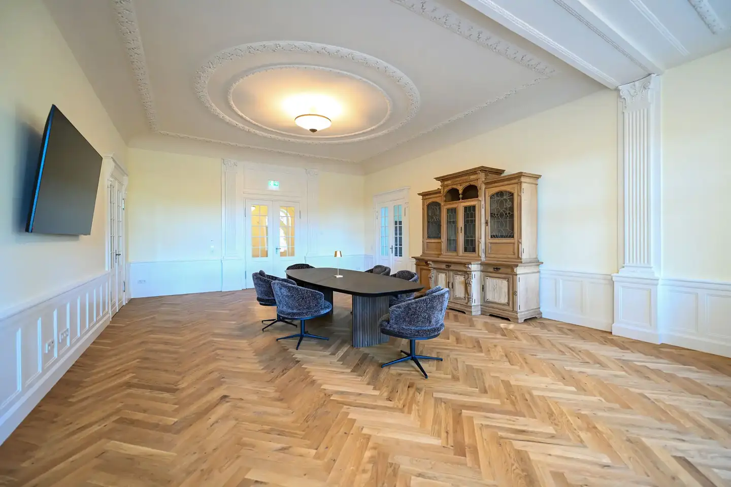 Stilvoller Gemeinschaftsraum in der Seniorenresidenz Lehnenhof mit historischem Stuck, modernem Konferenztisch, gemütlichen Sesseln und edlem Fischgrätparkett – barrierefrei und hochwertig ausgestattet.