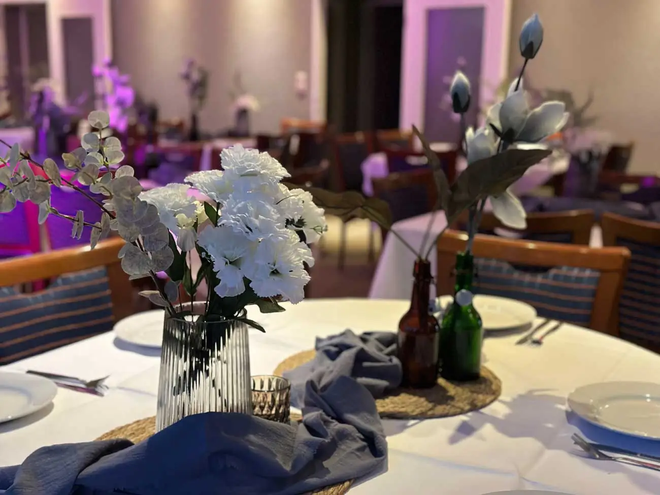 Heller, eleganter Veranstaltungsraum mit weißen Tischdecken und blumigen Dekorationen.