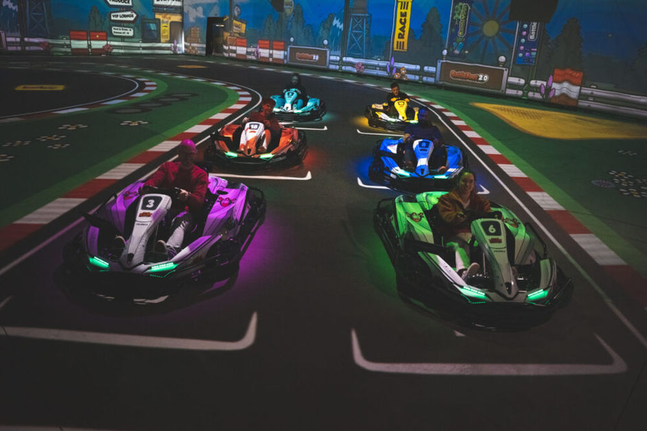 Rennfahrer in futuristischen E-Karts fahren auf einer interaktiven digitalen Rennstrecke mit bunten Lichteffekten. Das immersive Battle-Kart-Erlebnis kombiniert echtes Kartfahren mit virtuellen Gaming-Elementen für ein einzigartiges Rennabenteuer.