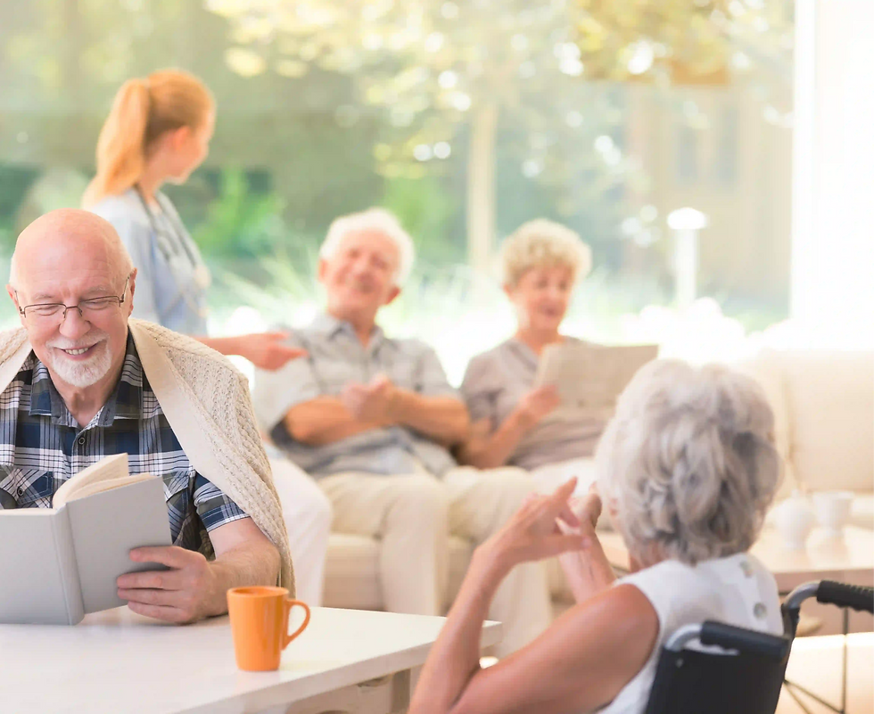 Seniorengruppe in heller, freundlicher Gemeinschaftslounge; eine Pflegekraft betreut im Hi