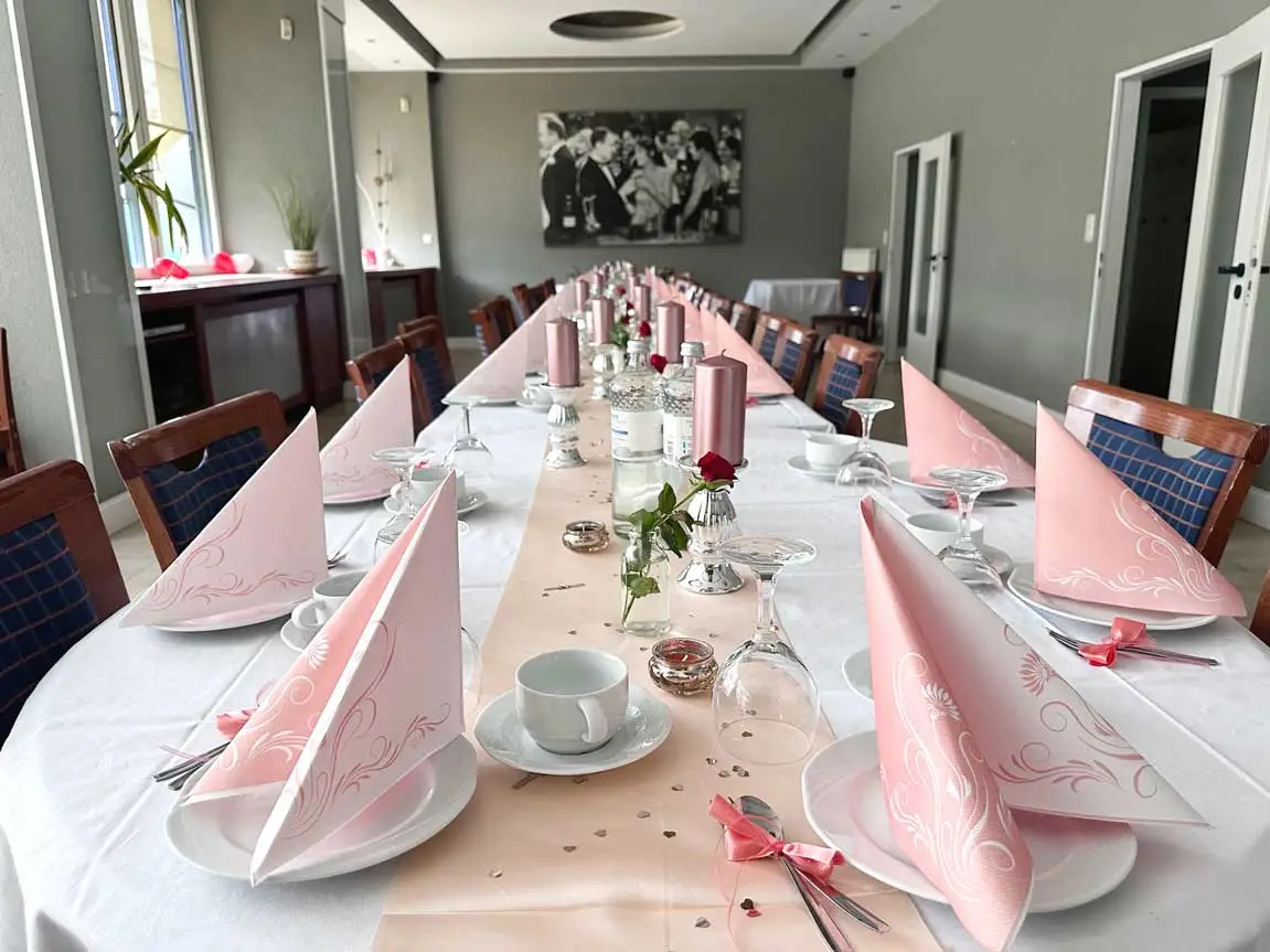 Festlich gedeckter Tisch mit rosa Servietten und Kerzen für eine Feier oder Veranstaltung.