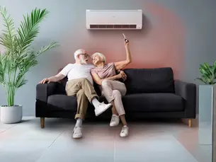 Älteres Paar sitzt entspannt auf dem Sofa unter einer modernen Klimaanlage – sichtbar angenehme Raumtemperatur durch gezielte Kühlung_