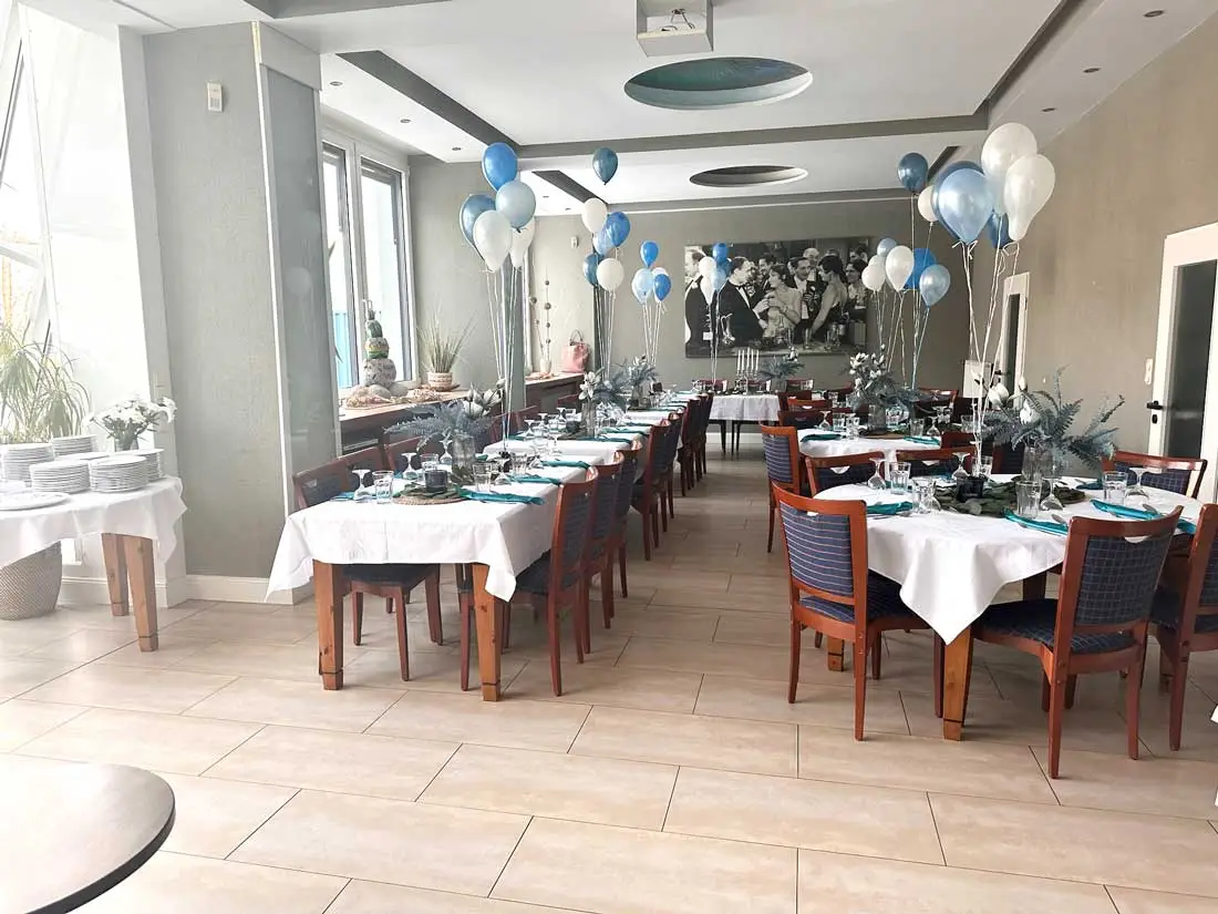 Ein langer Tisch in einem festlichen Raum, dekoriert mit weißen und blauen Luftballons.