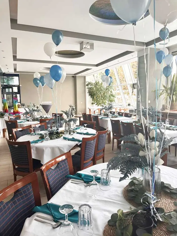 Festlich dekorierter Tisch mit blauen Luftballons und floralen Akzenten.