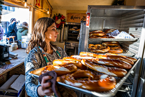Woman standing inside, while holding a tray of baked pretzels and other baked goods