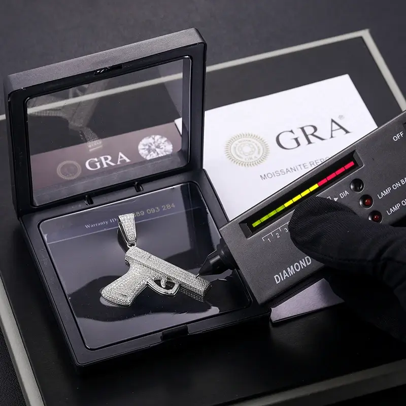 Thumbnail: Hand holding diamond tester, testing silver gun pendant with GRA certification.