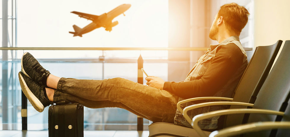 Man relaxes in airport lounge, legs on suitcase, holding phone. Airplane seen through window. Warm sunlight creates a calm mood.