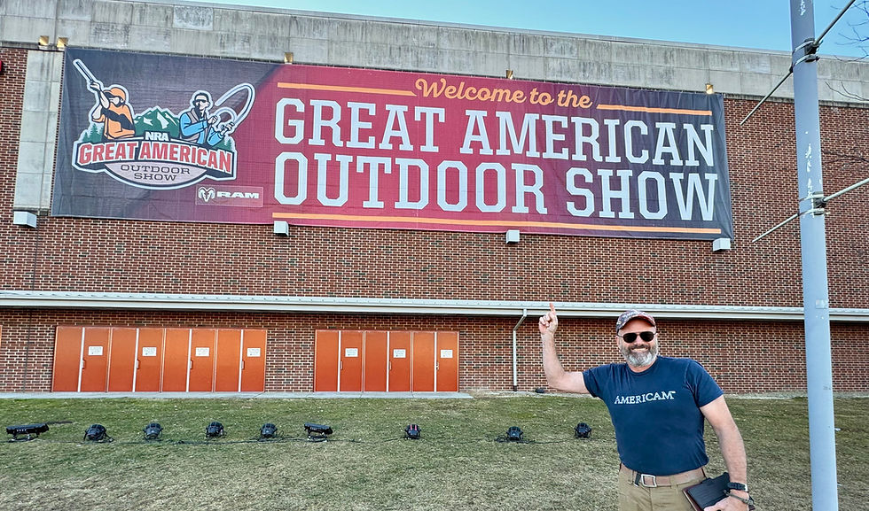 Americam Partner pointing to a building with a large sign welcoming people to the NRA's great american outdoor show
