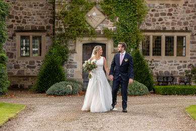 Newly weds holding hands, walking in the gardens at The Courtyard Venue in Oswestry. They are walking and chatting. they look happy and are surround by grass and greenery.