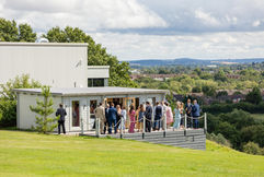 Guests are stood on the patio at Hencote, they are smiling and drinking. They are surrounded by Shropshire views and greenery.