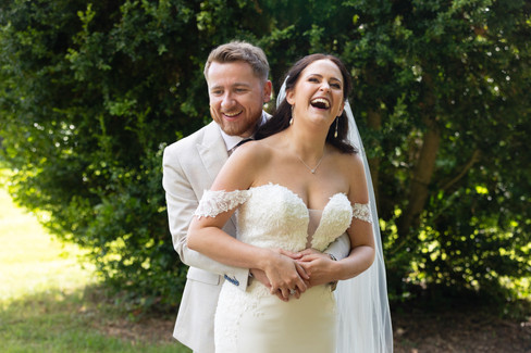 Groom holding his wife around the waist and both are laughing. Taken by Nicki Jones Photography at Netley Hall in Shrewsbury. 