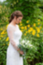 Bride in a white dress holds a bouquet, standing in front of vibrant yellow flowers in the gardens at Bromwich Park Farm in Oswestry. Greenery surrounds her, creating a relaxed setting.
