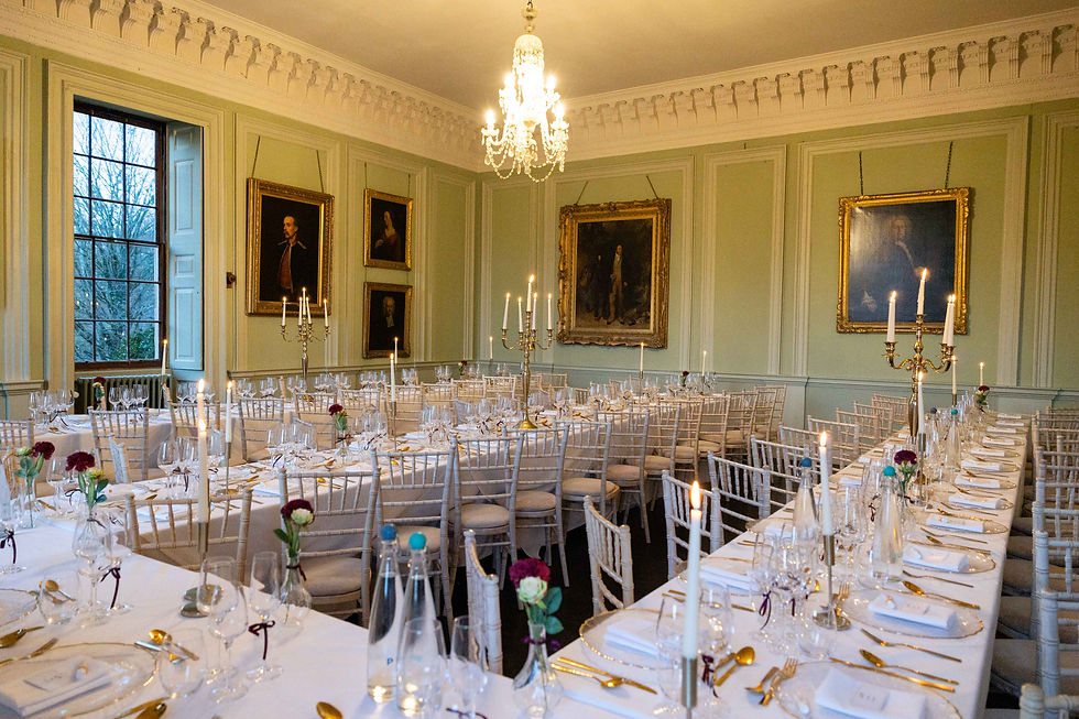Elegant dining room at Davenport House set for a wedding with long tables, white chairs, and gold cutlery. Chandeliers and paintings adorn the green walls.