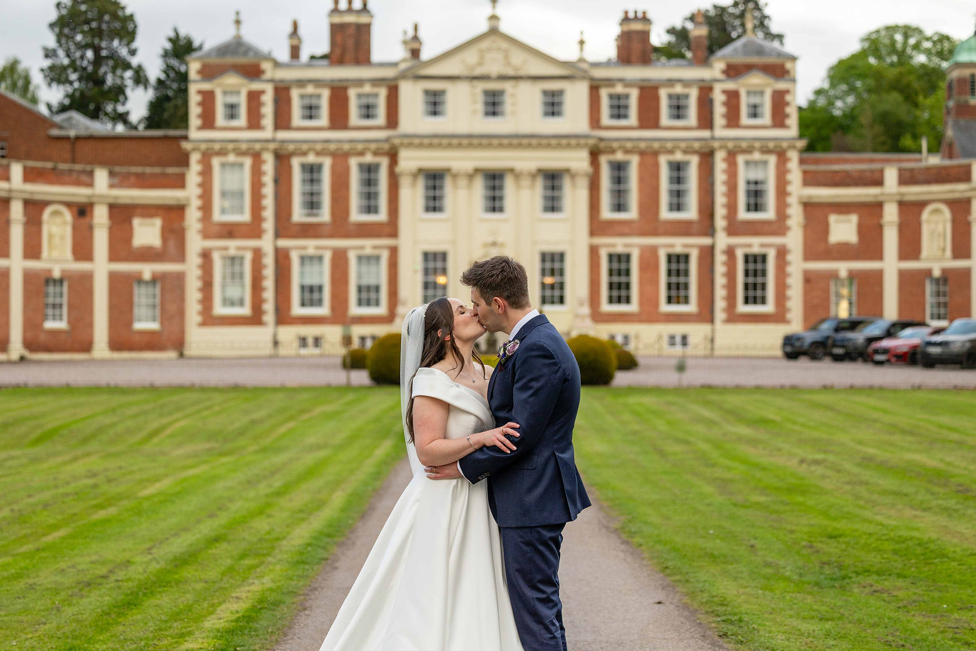 Newly married couple embrace and hold each other while stood outside the front door of Shropshire wedding venue - Hawkstone Hall. 