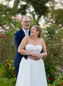 Newly married couple, hugging, and laughing. They are surrounded by dby greenery ans summer flowers. A natural, candod photo taken by Nicki Jones.