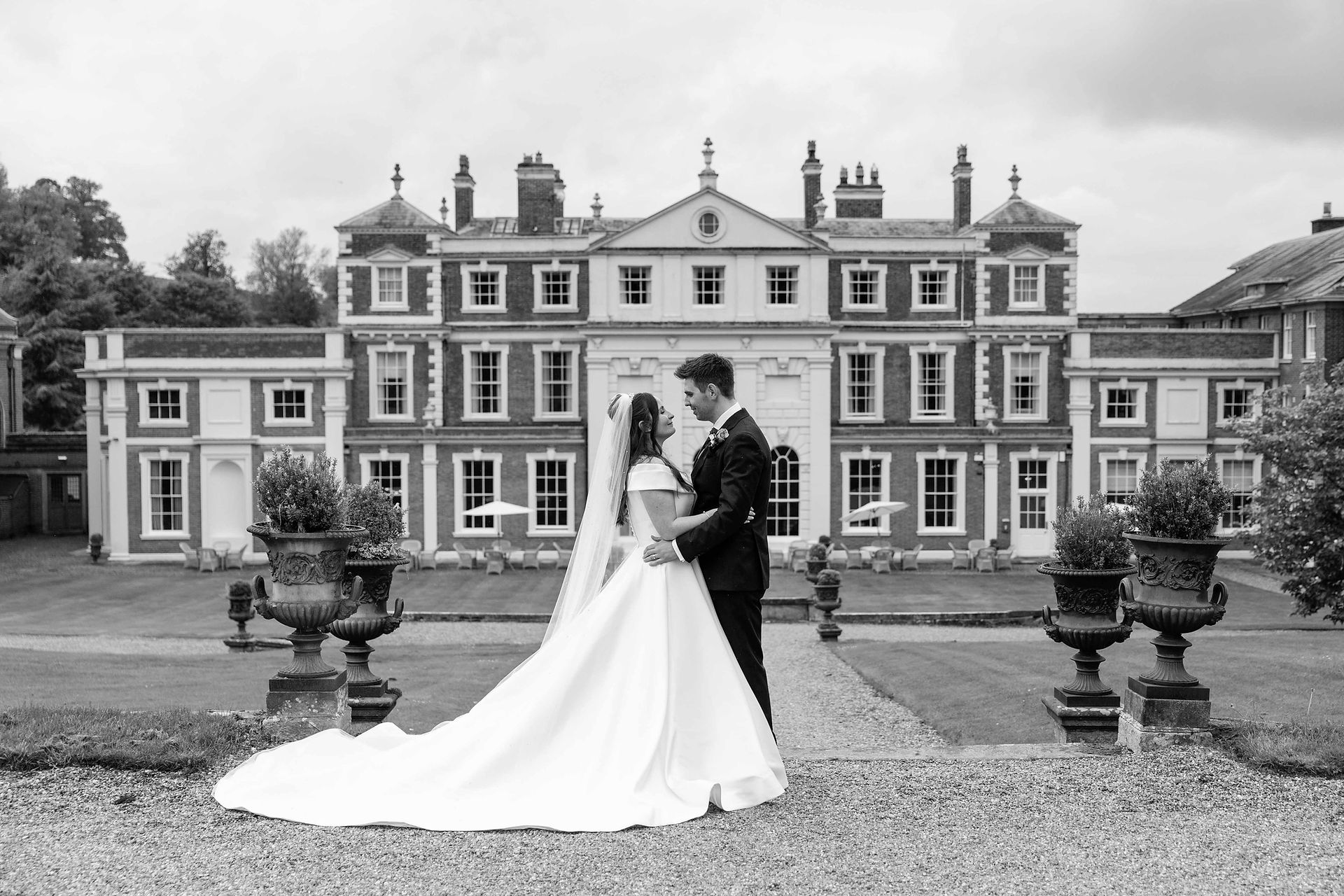 Newly married couple embrace outside the back of Hawkstone Hall. It is a black and white photo.