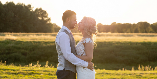 Bride and groom hold each other while looking at each other. They are surround by fields and greenery and are bathed in a beautiful golden light. 