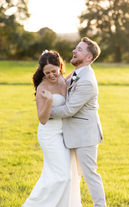 Newly weds enjoying a moment together, they are laughing and surrounded by golden sunlight and are in a rural setting.