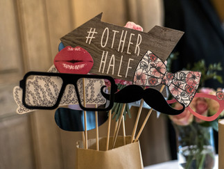 Wedding photo booth props in a bag, including glasses, bow ties, a moustache, and a sign reading “#OtherHalf”
