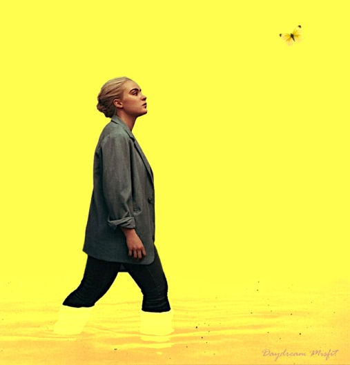 A blonde woman in a grey jacket and black leggings steps boldly through a pool of yellow against a background of a yellow sky and liquid sunshine while staring intently at a yellow butterfly.