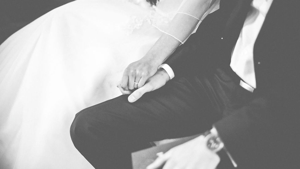 Black-and-white close-up of a bride and groom holding hands in a wedding scene, with the bride’s white dress and groom’s dark suit visible