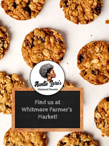 Several scattered oatmeal raisin cookies surrounding a chalkboard sign inviting customers to find Auntie Lara's Oatmeal Sweets at the market