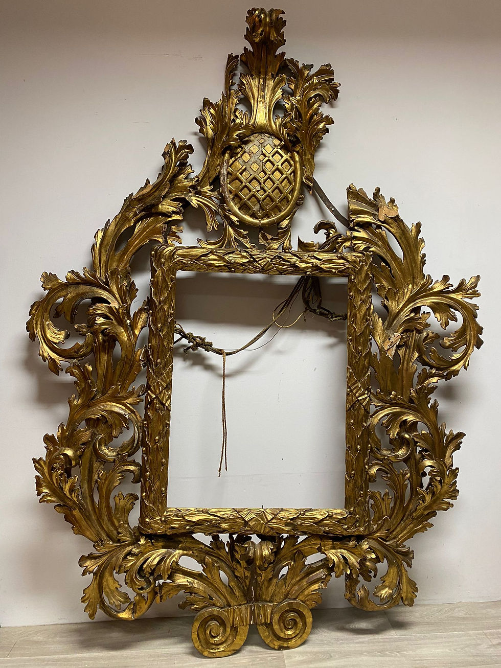 Es handelte sich um einen über 2 Meter hohen antike Barockrahmen, der von der Wand gefallen war. Die Verzierungen der rechte Seite waren gänzlich vom Rahmengestell gelöst und viele Teile waren heraus gebrochen. Ziel war es, den Rahmen zu stabilisieren, alle Teile wieder an ihren Platz zu bringen, fehlende Teile zu ergänzen und an die vorhandene Oberfläche anzugleichen. Außerdem sollte die Krone gekürzt werden.