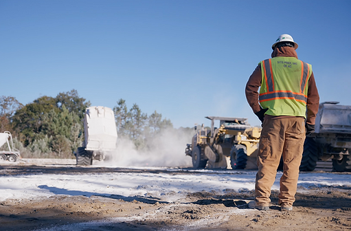 Construction worker with high visibility vest and hard hat watching a work truck dispense calcified lime.
