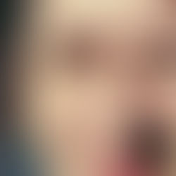 Nahaufnahme einer Frau, die in grellem Sonnenlicht die Augen zusammenkneift; dunkles Haar, grüne Ohrringe, kichernder Blick.