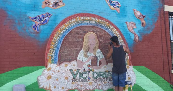 A volunteer studies Victoria's portrait as he adds details to the mural