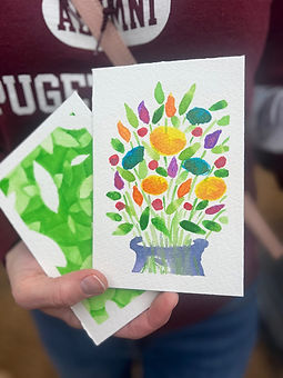 Hand holding two cards, one with a colorful bouquet in a blue vase and one with a leafy green design.