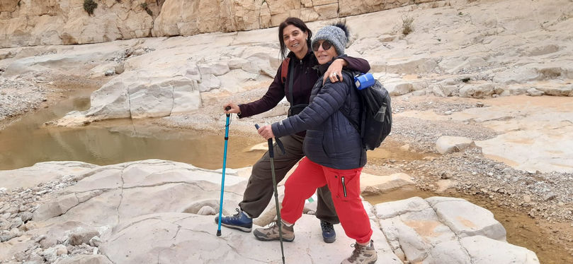 2 מטיילות בגבים בנחל צאלים עם מקלות ותרמיל וכובע צמר