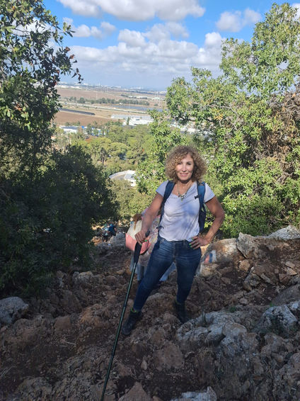 מטיילת עם תרמיל על הגב מחייכת למצלמה ליד עציי חורש בכרמל