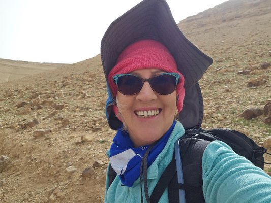 מטיילת מאירה אור-לבן במדבר עם משקפיי שמש כובע חם וכובע מג שמש