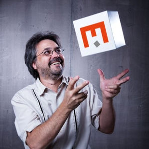 Stephen Benedetti headshot wearing glasses and a white shirt and tossing a white cube with a red letter E on it