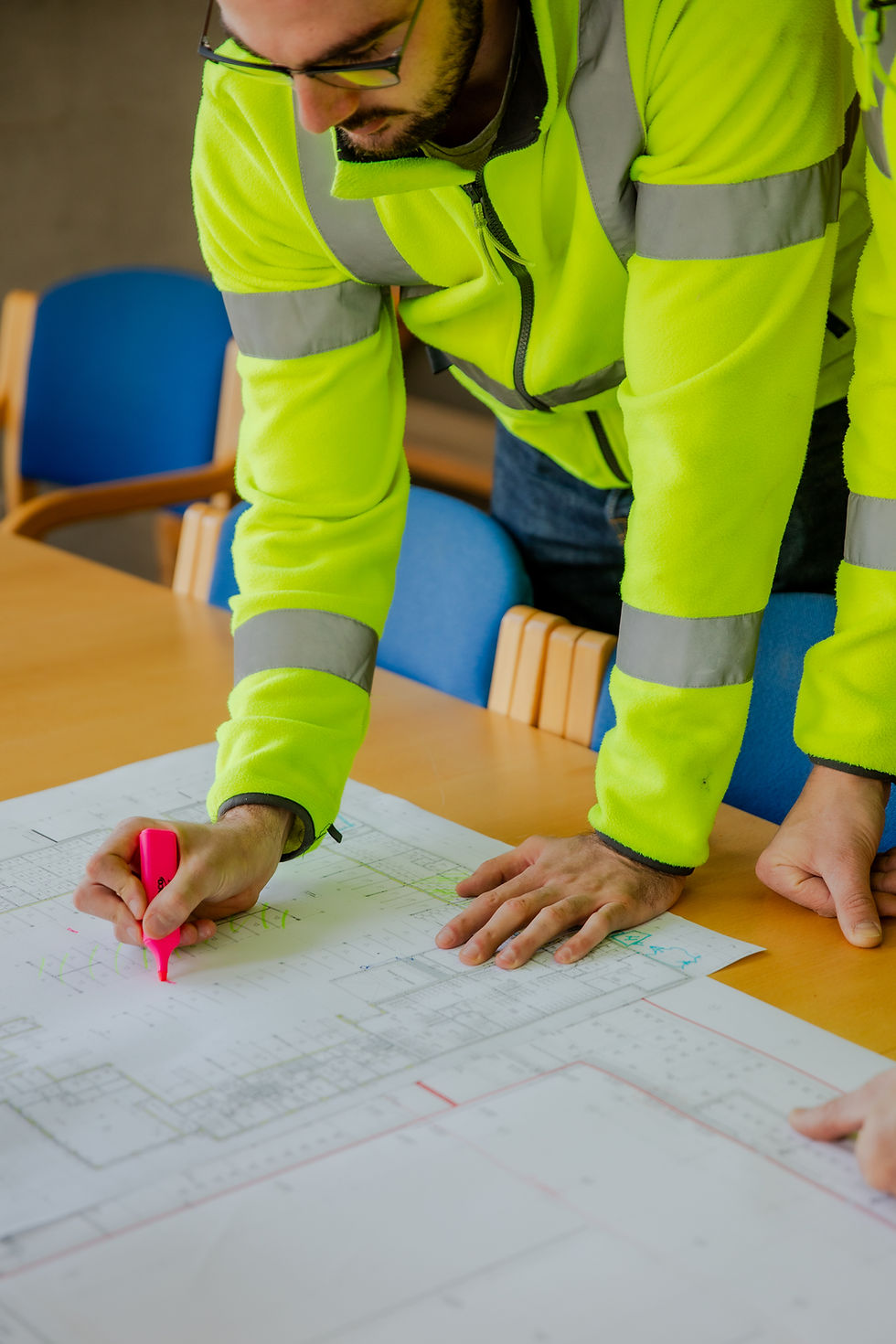 Worker in high-visibility jacket reviewing blueprints.
