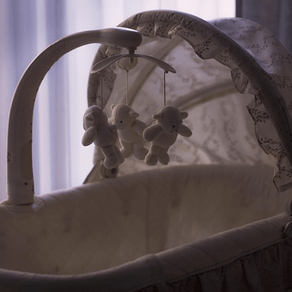 In a dimly lit room, an empty crib quietly stands with toy bears gently hanging above, symbolising a poignant reminder of miscarriage, pregnancy loss and unfulfilled dreams of parenthood.
