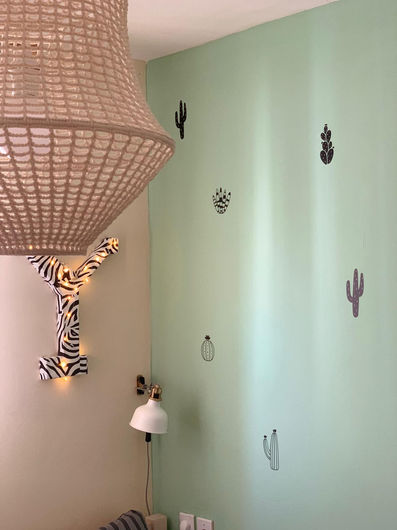 מנורת קש מעוצבת עם מדבקות קקטוסים על קיר ירוק בהיר